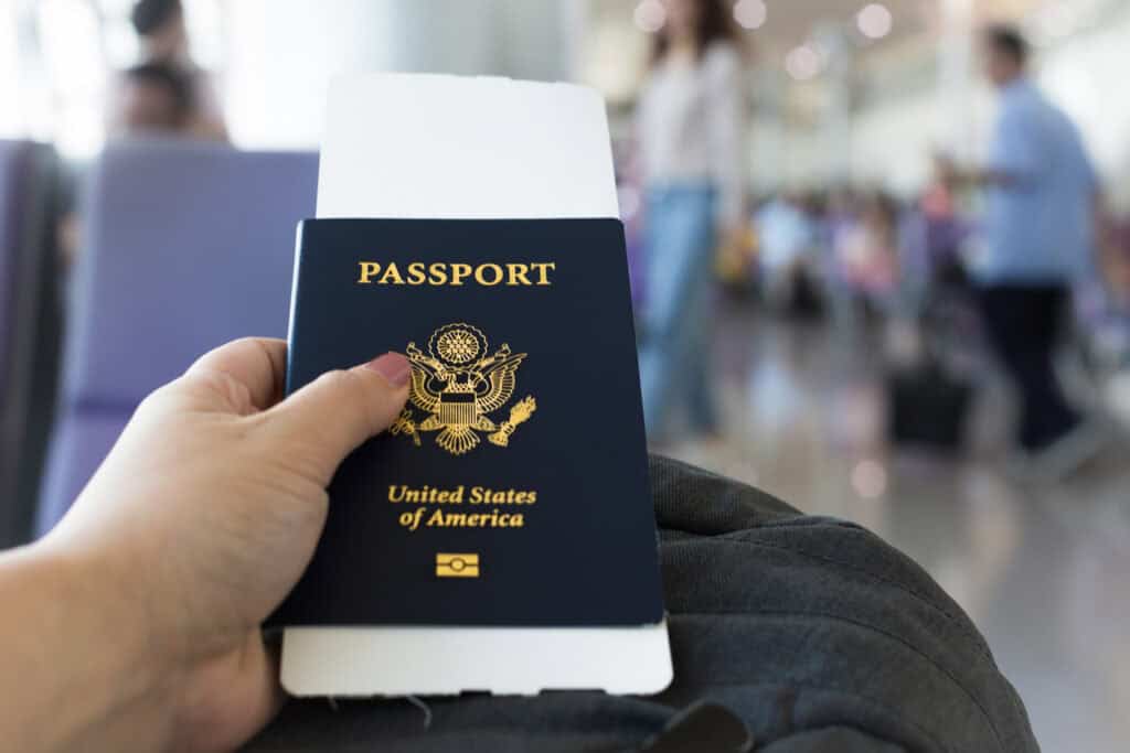 White hand holds an American passport while sitting in an airport terminal