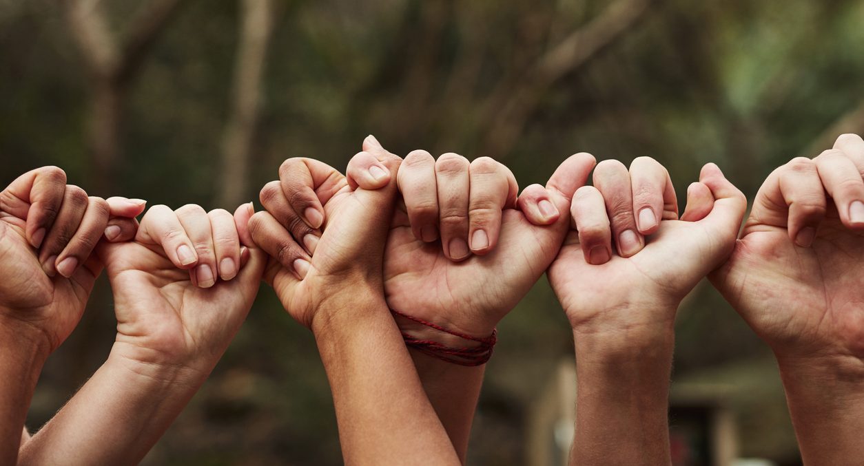 Cropped shot of a group of people linking fingers out in nature. Only their hands are shown.