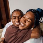 A Black transgender woman and her Black trans masc lover embrace each other.