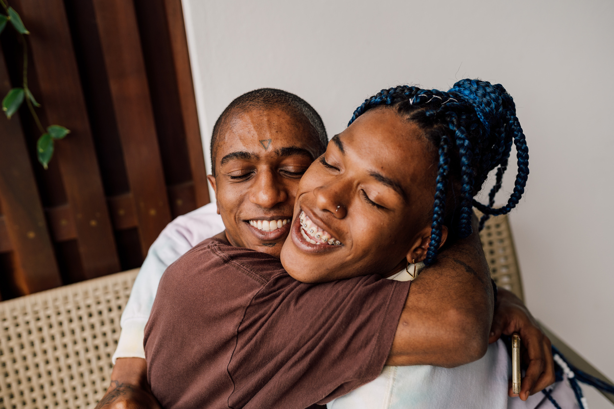 A Black transgender woman and her Black trans masc lover embrace each other.