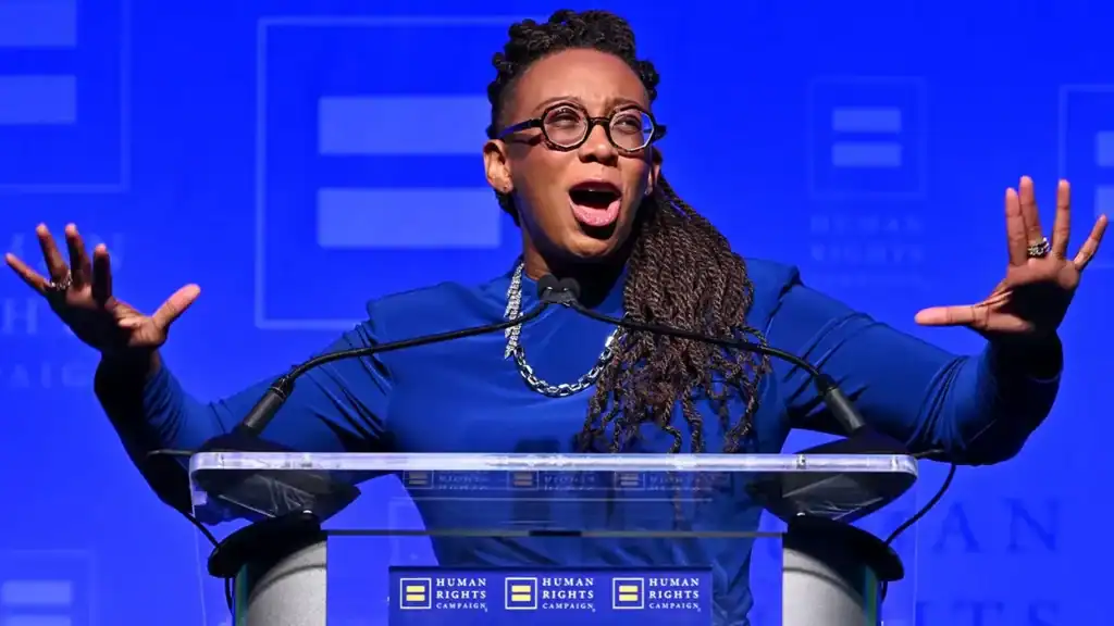 HRC president Kelley Robinson, a black woman in a silk shirt, speak animately at a Human Rights Campaign podium