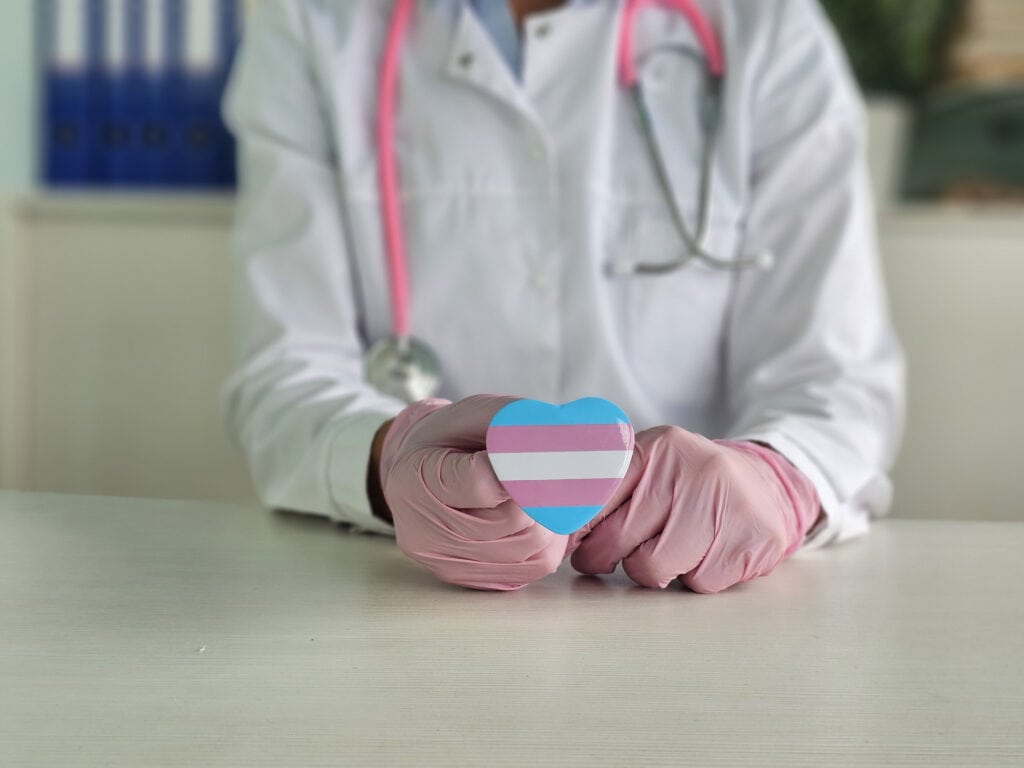 Healthcare professional holds a pink and blue heart symbolizing transgender pride in a medical office setting