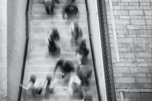 A black and white aerial view photo of people walking up and down a staircase. The bodies are blurred.